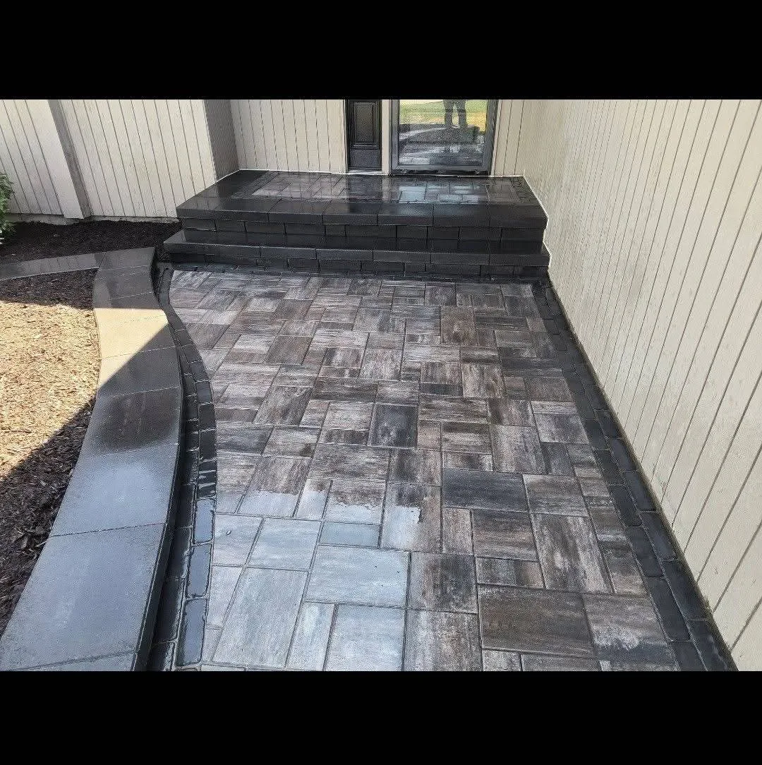 Dark gray paver patio laid in a herringbone pattern alongside a home