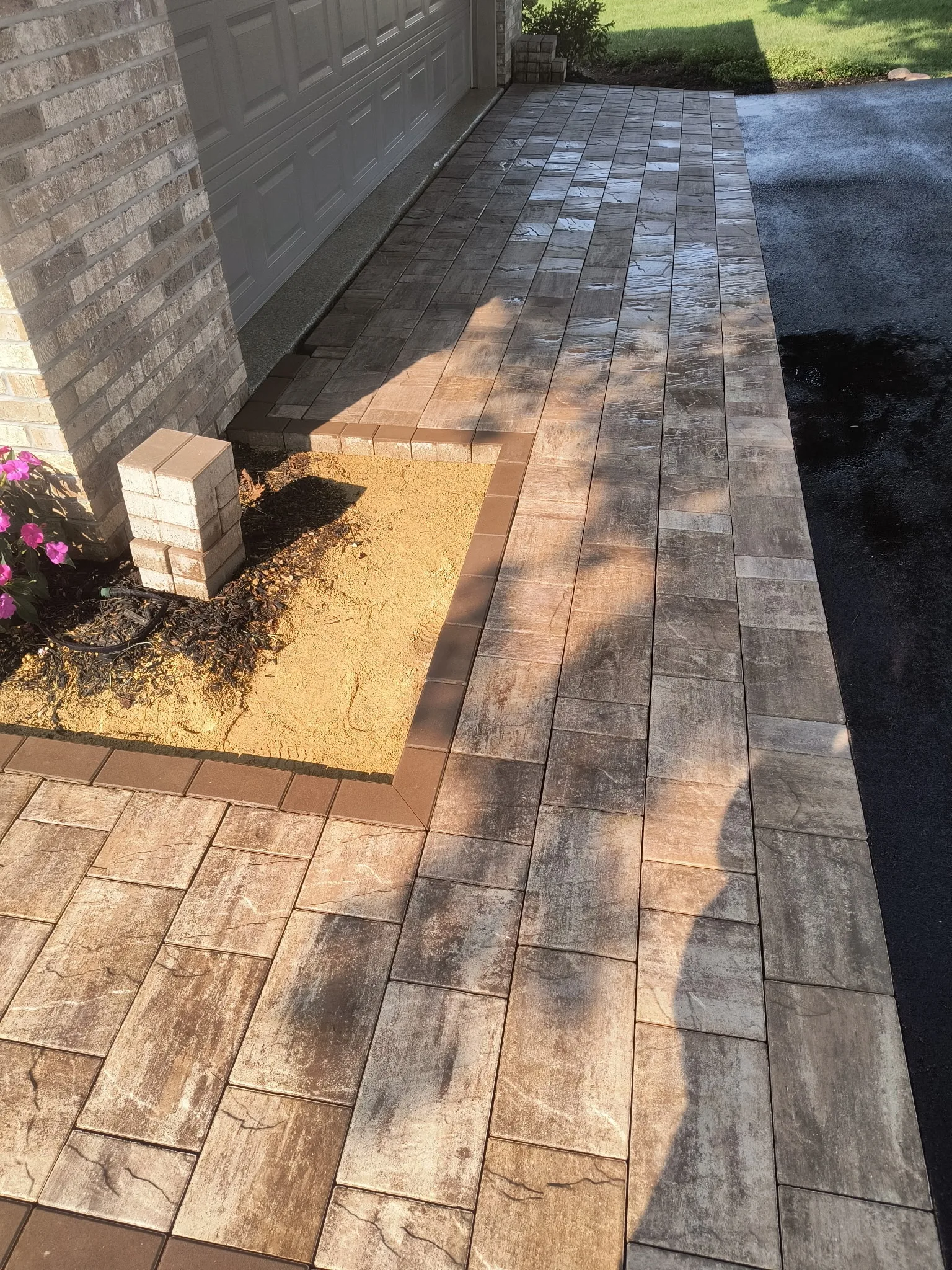 Decorative paver driveway in a wood-grain pattern leading to a garage, with a planted bed alongside