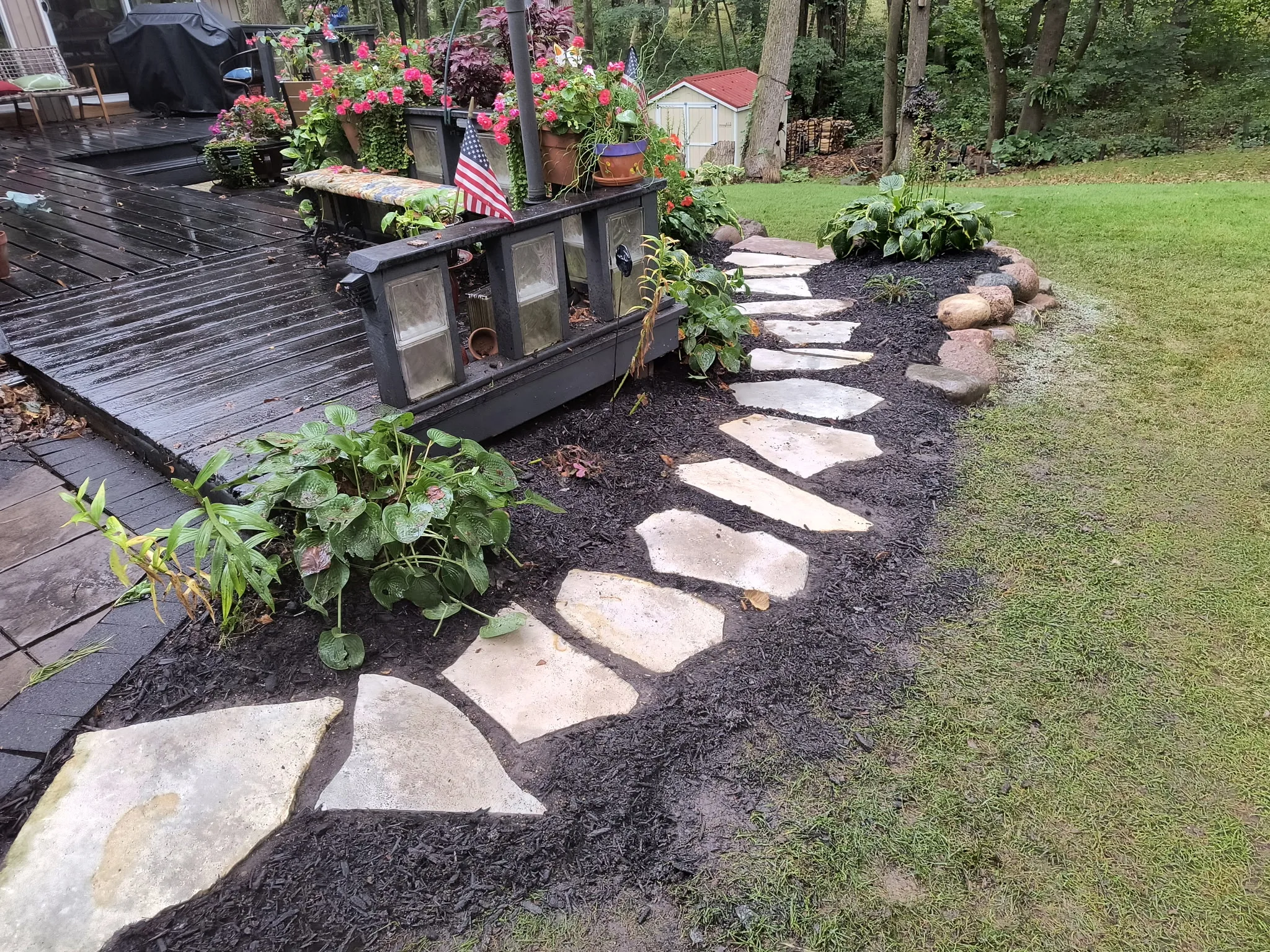 Flagstone pathway through dark mulch beds with planters and hostas in a finished backyard