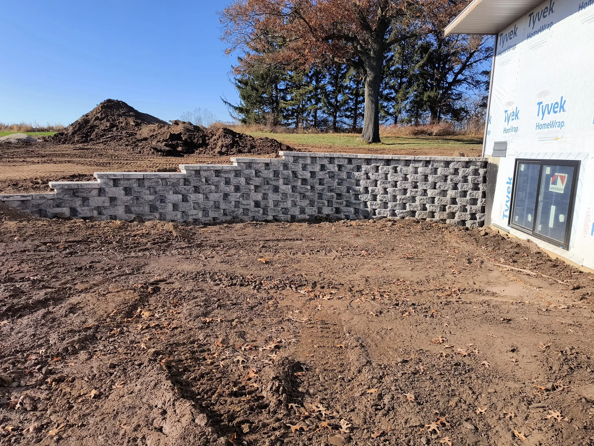 Concrete retaining wall under construction beside a building, with mulch piles and bare ground on site